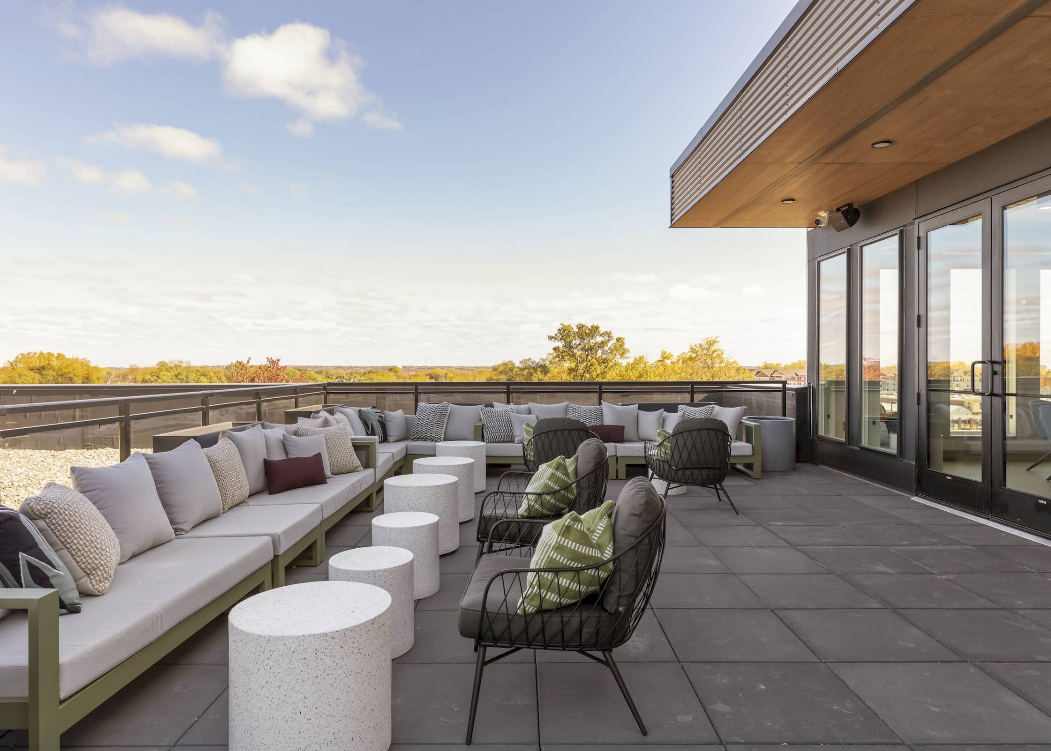 Modern rooftop patio with cushioned seating, small round tables, and a scenic view under a partly cloudy sky.