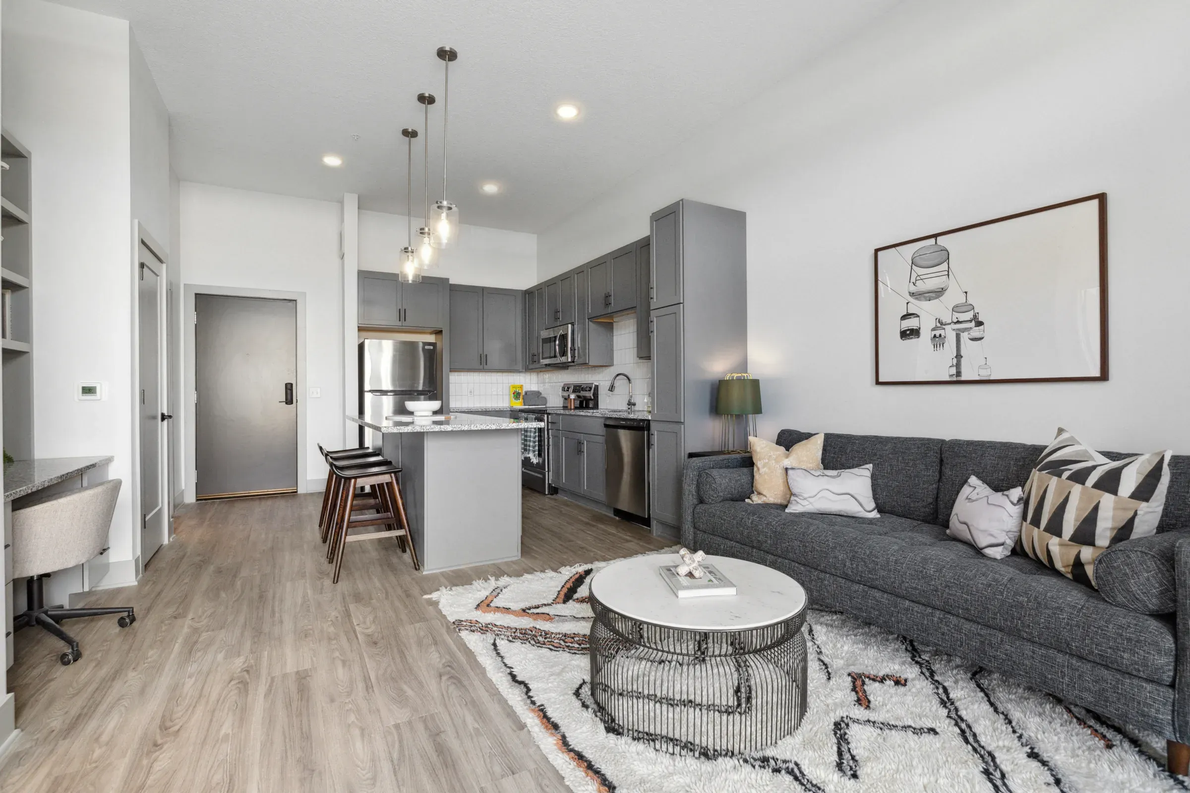 Savor Apartments Modern open-plan kitchen and living room with gray cabinets, gray sofa, and decorative accents.