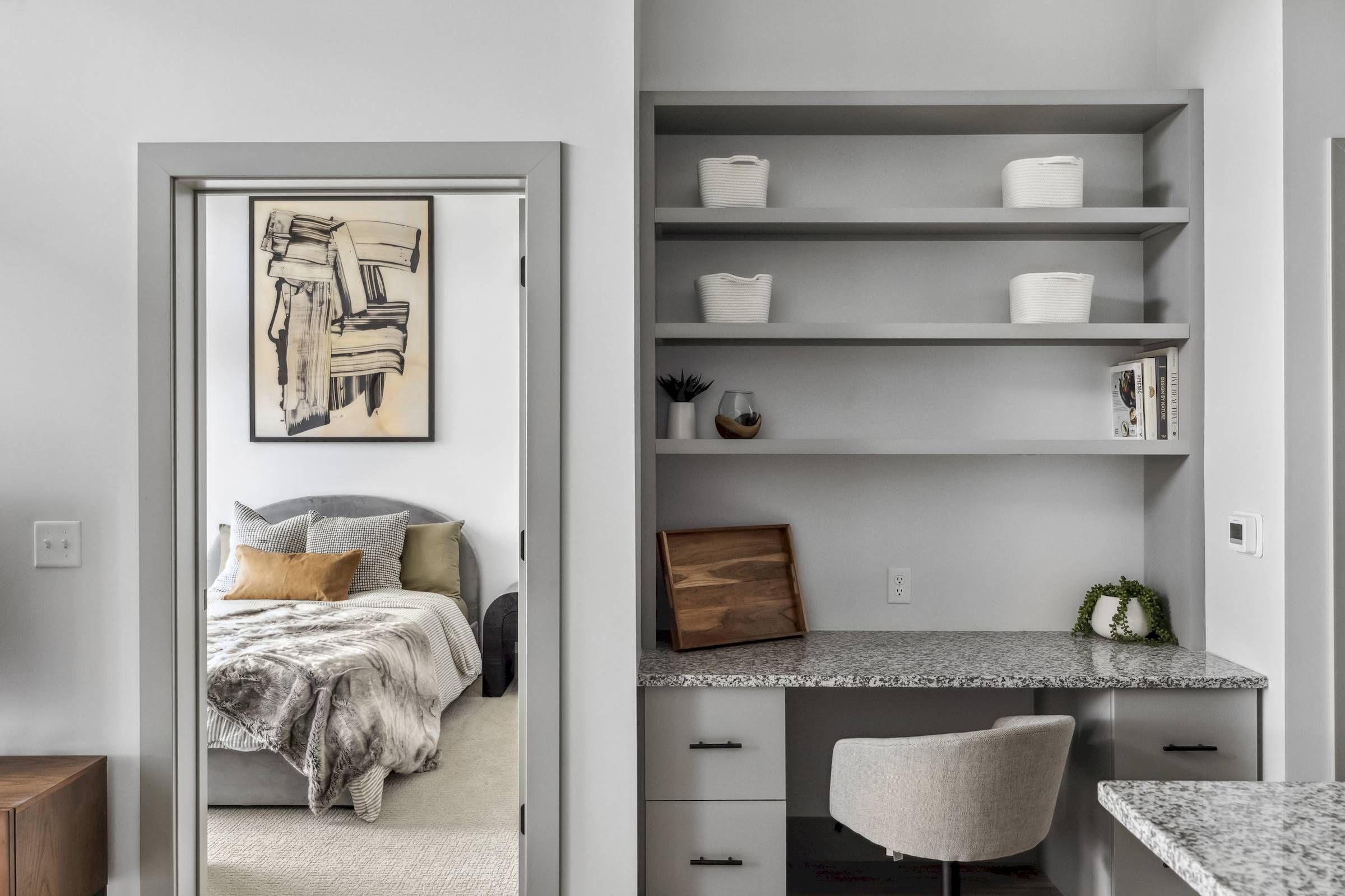A modern home office with built-in shelves, next to a cozy bedroom with abstract art above the bed.
