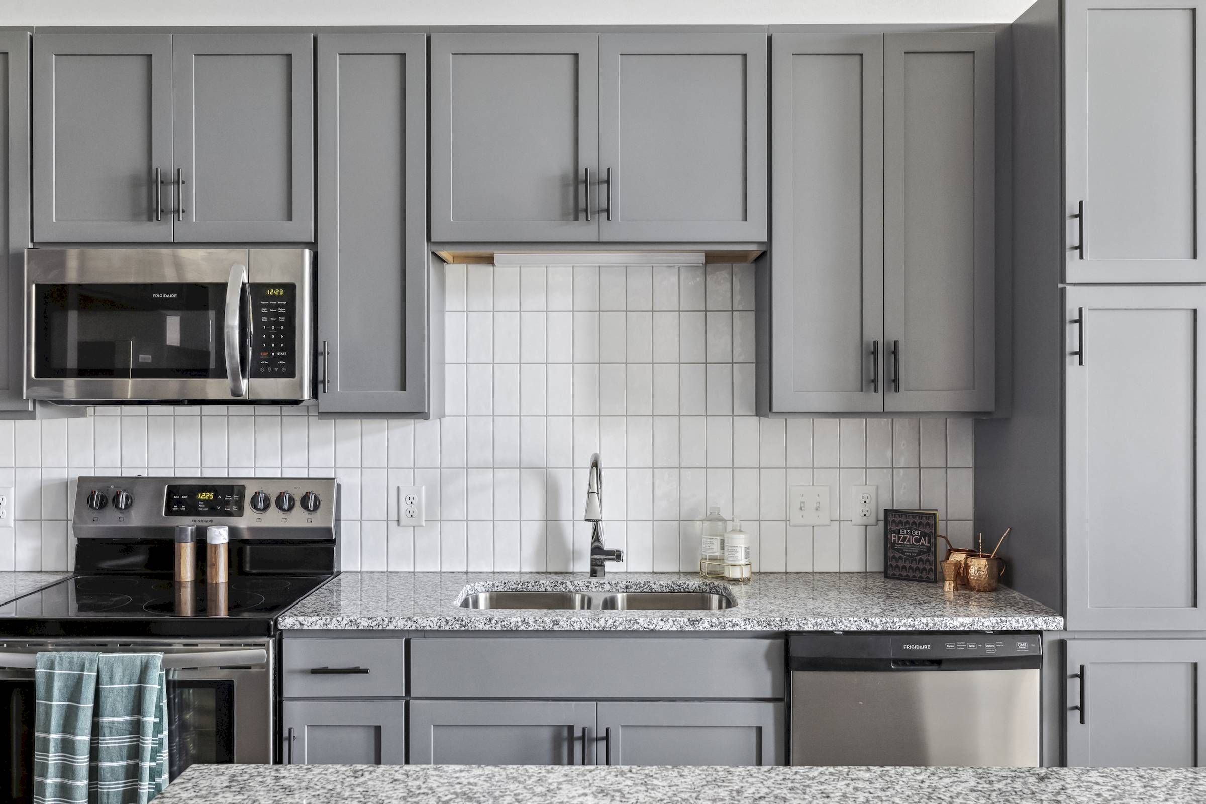 Modern kitchen with gray cabinets, stainless steel appliances, and a white tiled backsplash.