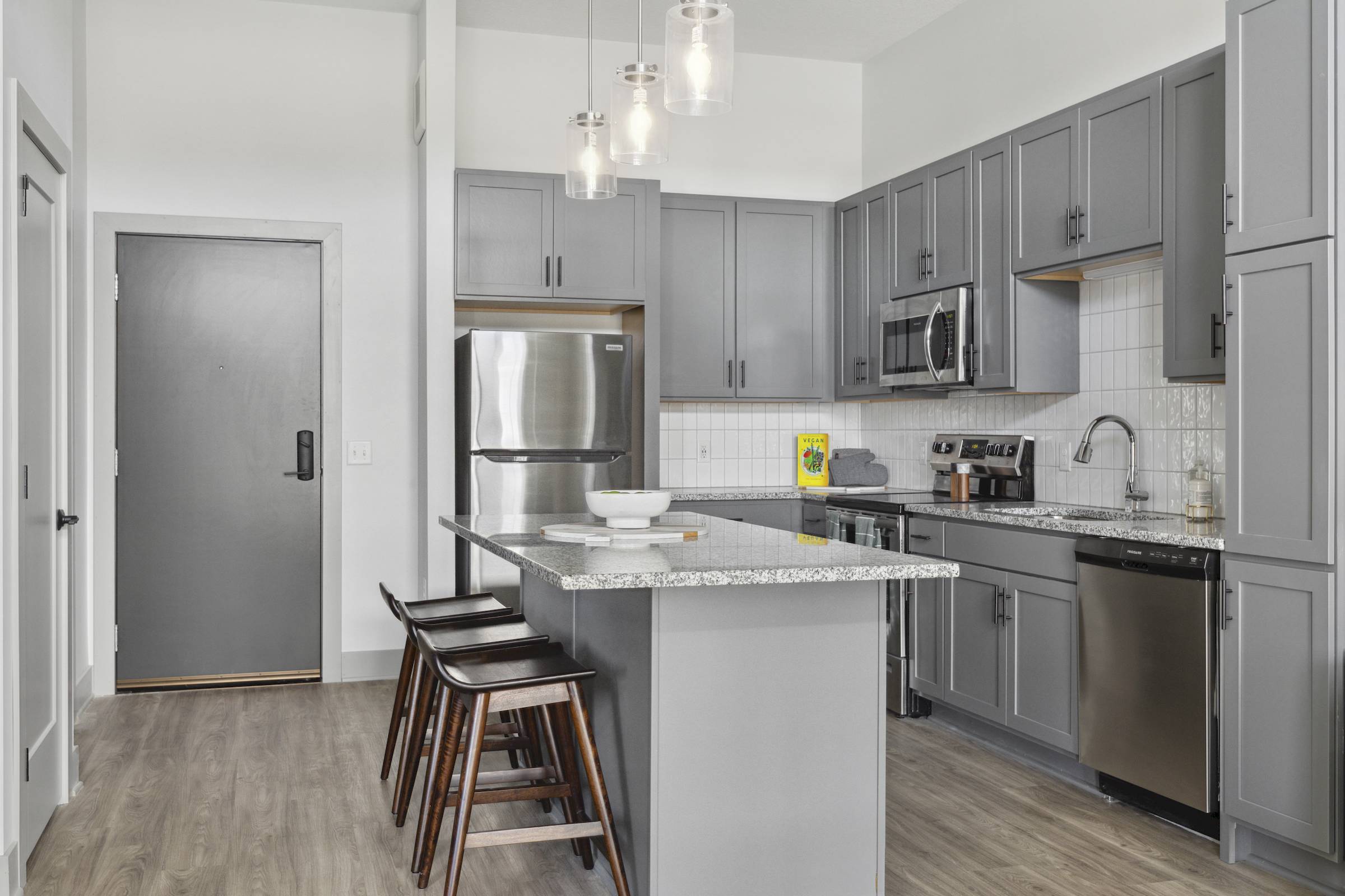 Modern kitchen with gray cabinets, stainless steel appliances, and a granite island with wooden stools.