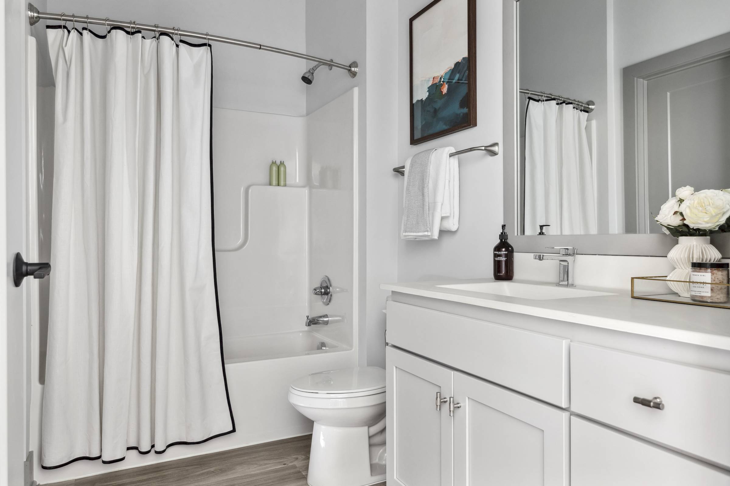 White bathroom with a shower curtain, toilet, sink, mirror, and decorative items on the counter.